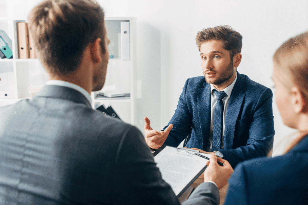 Man in a navy blue suit being interviews for a job by a male and female recruiter.